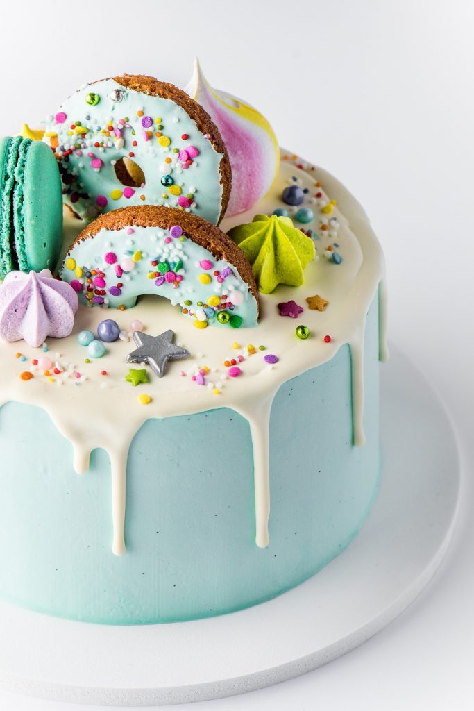A light blue cake with donuts and sprinkles on the top.