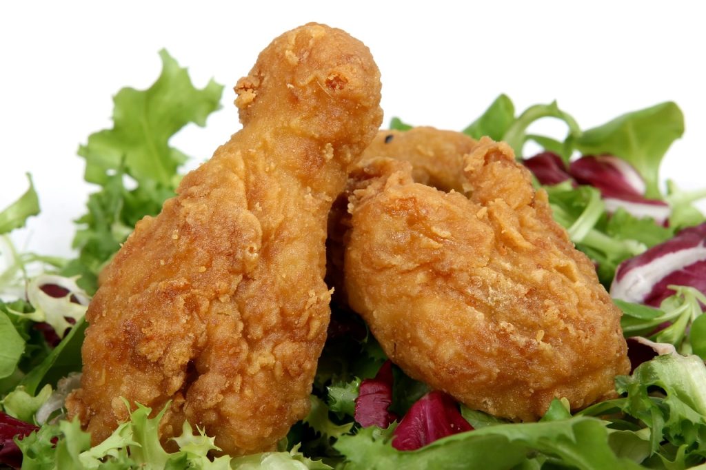 Two pieces of fried chicken legs on a bed of lettuce.